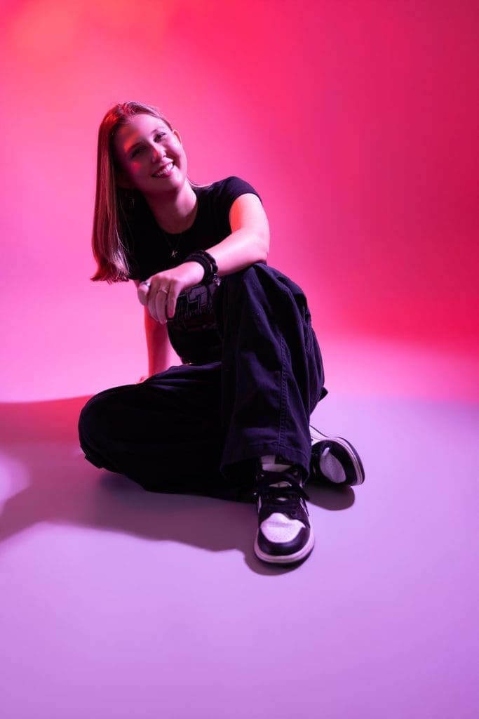 KKRuby16thBday Creative teen portrait in a pink and purple neon-style set: seated girl in black with a skater street vibe concept.