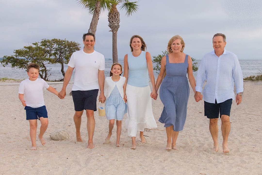 Family walking hand in hand on a sandy beach near palm trees during a coastal portrait session