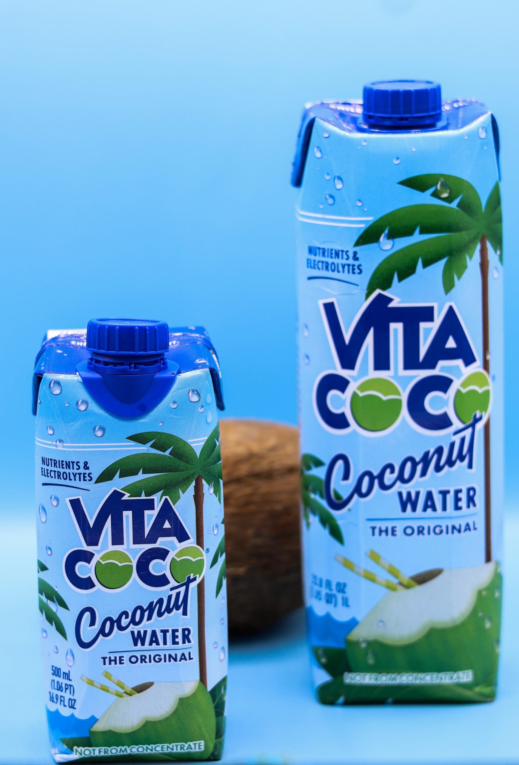 A commercial photography image of two vita coco waters on a bright blue backdrop with a coconut.