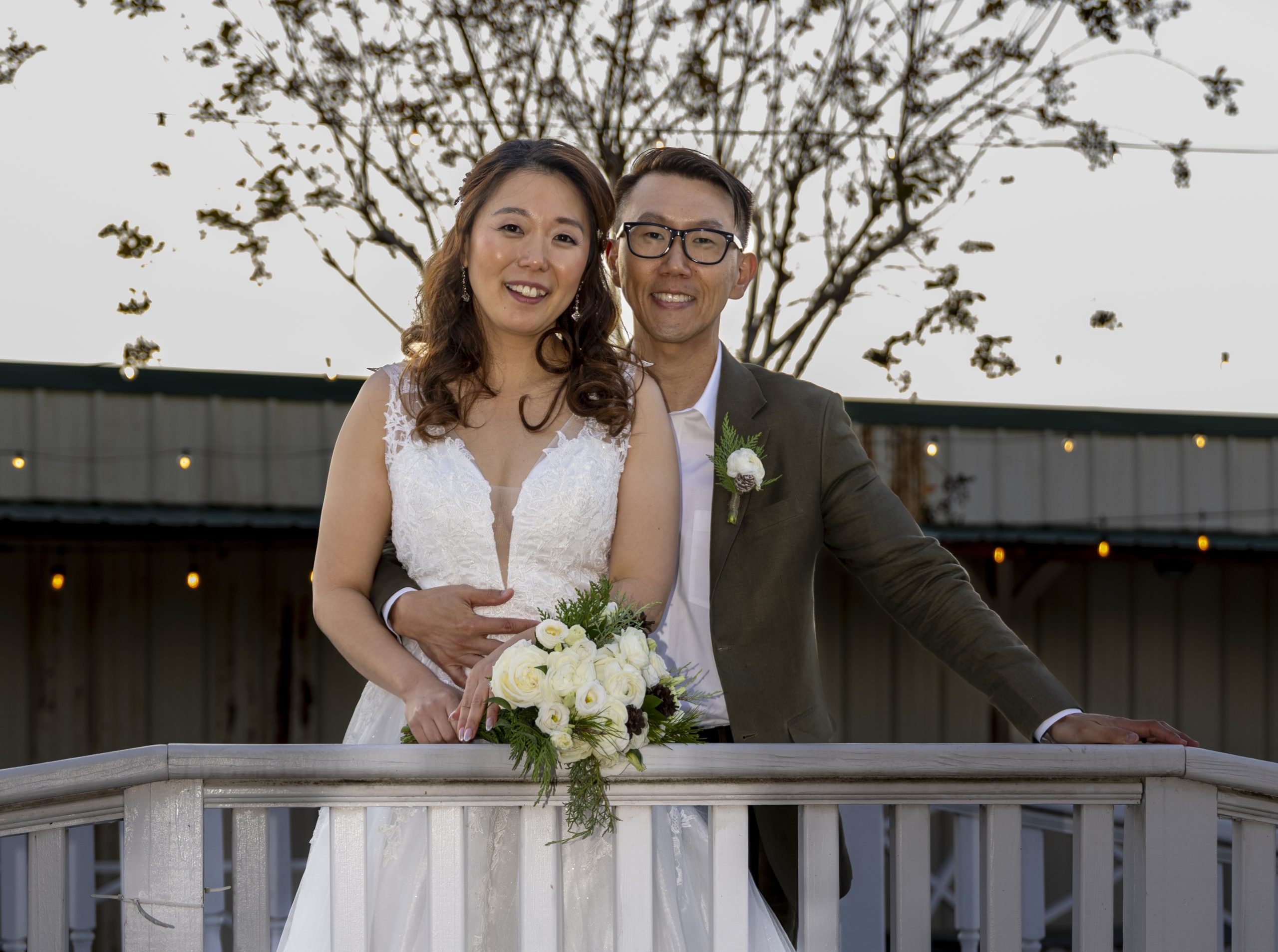 An Asian couple poses on a wooden bridge after their wedding ceremony.